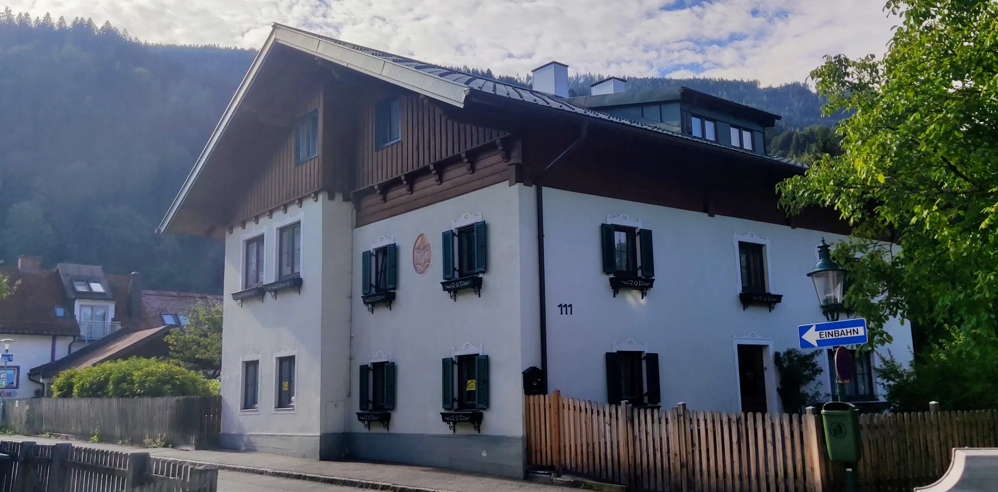 Die Alte Hafnerei in Schladming: ein weiß verputztes Haus mit grünen Fensterläden und Holzgiebel vor bewaldeten Bergen