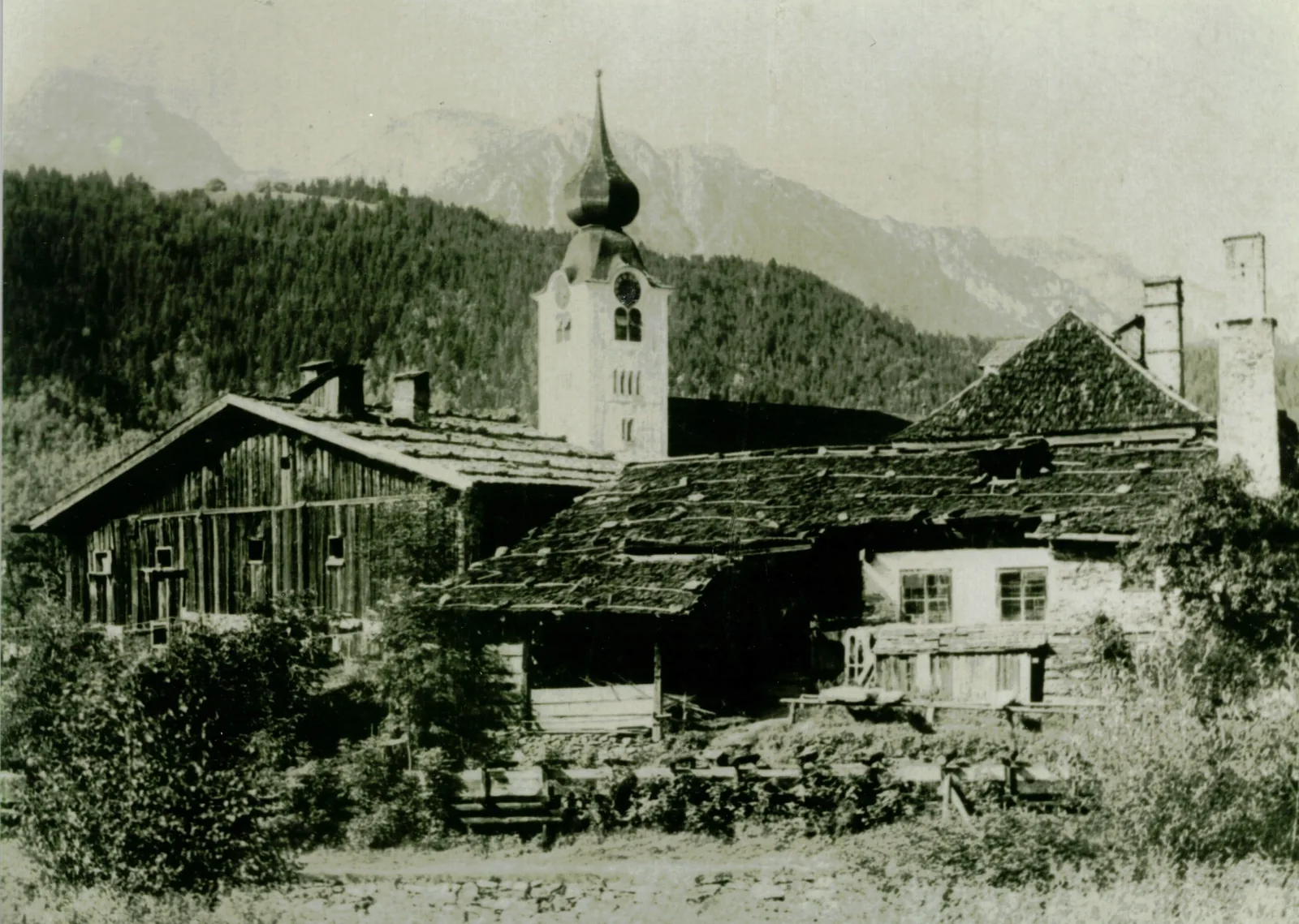 Historische Schwarz-Weiß-Aufnahme alter Holzhäuser in Schladming mit Zwiebelturm der Kirche und Bergen im Hintergrund